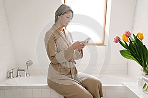 Mature grey woman using mobile phone in bathroom