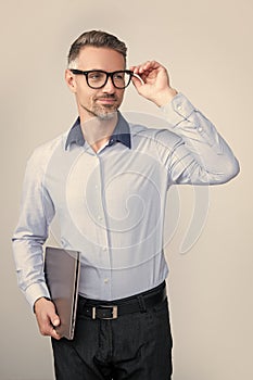 mature grizzle man in eyeglasses hold pc on grey background