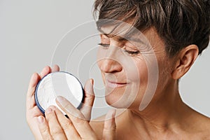Mature half-naked woman smiling while applying face cream