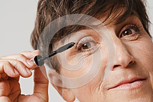 Mature half-naked woman smiling while applying mascara