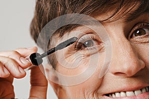 Mature half-naked woman smiling while applying mascara