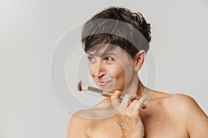 Mature half-naked woman smiling while posing with powder brush