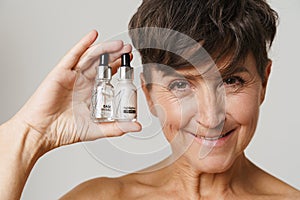 Mature half-naked woman smiling while showing cosmetic products