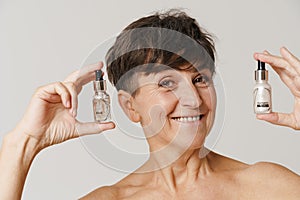 Mature half-naked woman smiling while showing cosmetic products