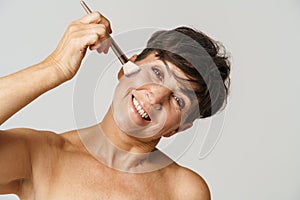 Mature half-naked woman smiling while using powder brush