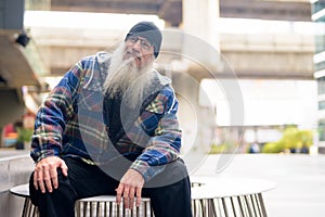 Mature handsome bearded man sitting and thinking outdoors