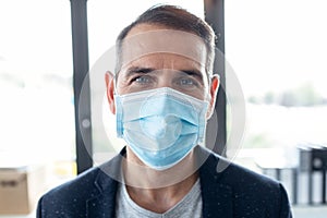 Mature handsome man wearing an hygienic mask to prevent others from a virus while looking at camera in the office