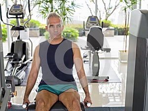 Mature handsome Persian man doing leg extension exercise at the gym