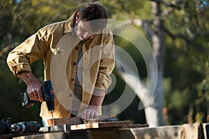 Mature handyman carpenter working in carpentry diy workshop outdoors with drill.