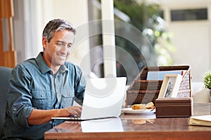 Mature Hispanic Man Using Laptop On Desk At Home