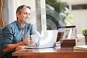 Mature Hispanic Man Using Laptop On Desk At Home