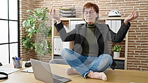 Mature hispanic woman business worker doing yoga meditation on the table at office