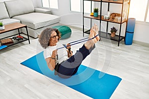 Mature hispanic woman doing exercise with elastic bands at the living room at home