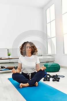 Mature hispanic woman doing yoga meditation at the living room at home