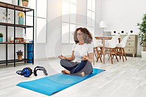 Mature hispanic woman doing yoga meditation at the living room at home