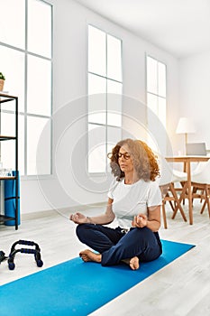 Mature hispanic woman doing yoga meditation at the living room at home