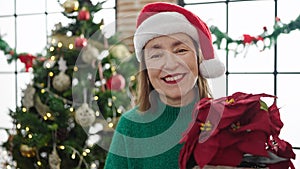 Mature hispanic woman with grey hair holding christmas plant at home