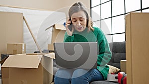 Mature hispanic woman with grey hair talking on smartphone using laptop at new home