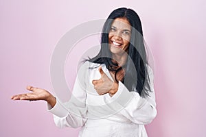 Mature hispanic woman standing over pink background showing palm hand and doing ok gesture with thumbs up, smiling happy and