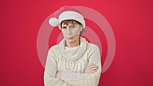 Mature hispanic woman standing upset wearing christmas hat over isolated red background