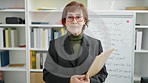 Mature hispanic woman teacher standing by white board with clipboard at library university