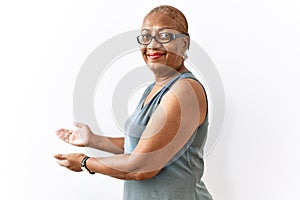 Mature hispanic woman wearing glasses standing over isolated background inviting to enter smiling natural with open hand