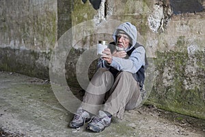 Mature homeless man sitting outdoors holding out a tin