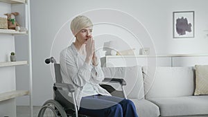 Mature hopeless woman in with spinal injury praying to Gao, sitting in wheelchair at home interior, empty space