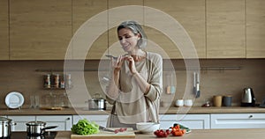 Mature housewife holds smartphone talking on speakerphone in the kitchen