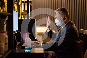 Mature Japanese businessman with mask video calling while working overtime at home late at night