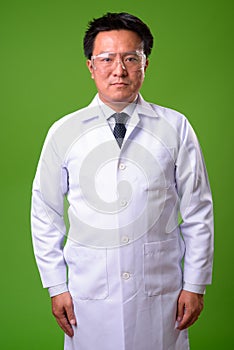 Mature Japanese man doctor wearing protective glasses against green background