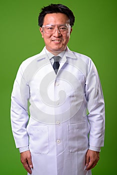 Mature Japanese man doctor wearing protective glasses against green background