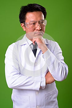 Mature Japanese man doctor wearing protective glasses against green background