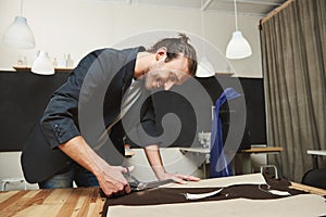 Mature joyful attractive dark-haired hispanic, male fashion designer working on new dress in workshop, cutting out parts