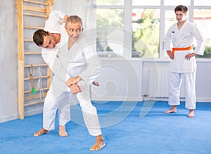 Mature judo fighters honing techniques during training bout in dojo