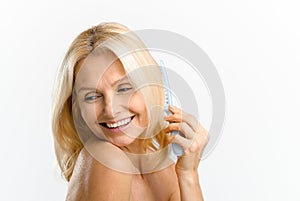 Mature lady caring her hair. Elegant serene middle-aged blonde woman combing with crest, looks down and smiling