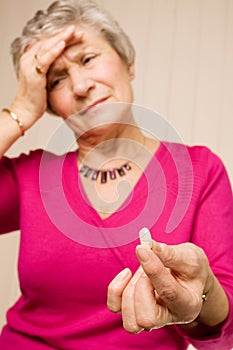 Mature lady with headache holding tablet or pill