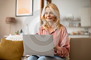 Mature lady holding laptop computer on lap working from home