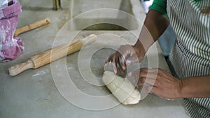 Mature Latin woman kneading flour dough with rolling pin in old vintage kitchen