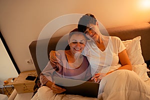 Mature lesbian couple hugging and using laptop in bed