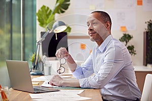 Mature Male Architect With Laptop Working In Office At Desk On Plans For New Building