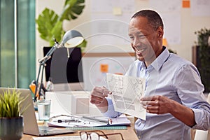 Mature Male Architect In Office Sitting At Desk Showing Plans For New Building On Video Call