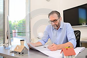 Mature male architect working on laptop on building project drawing sketch in office studio workspace