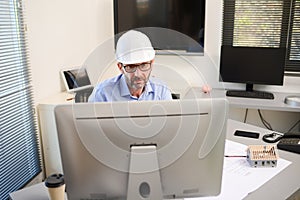 Mature male architect working on laptop on building project drawing sketch in office studio workspace