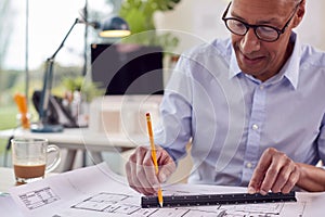 Mature Male Architect Working In Office At Desk On Plans For New Building