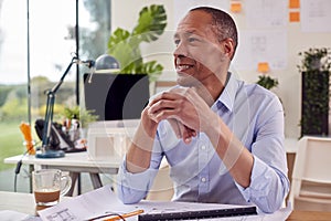 Mature Male Architect Working In Office At Desk On Plans For New Building