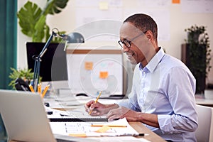 Mature Male Architect Working In Office At Desk Studying Plans For New Building