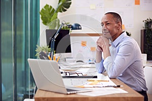 Mature Male Architect Working In Office At Desk Working On Plans For New Building