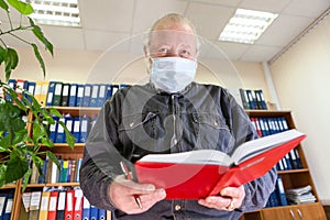 Mature male archivist holding open red notebook in hands, looking at camera, man wearing face mask due Covid-19 pandemic