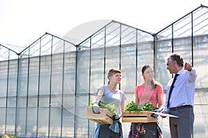 Mature male biochemist discussing with female coworkers against greenhouse